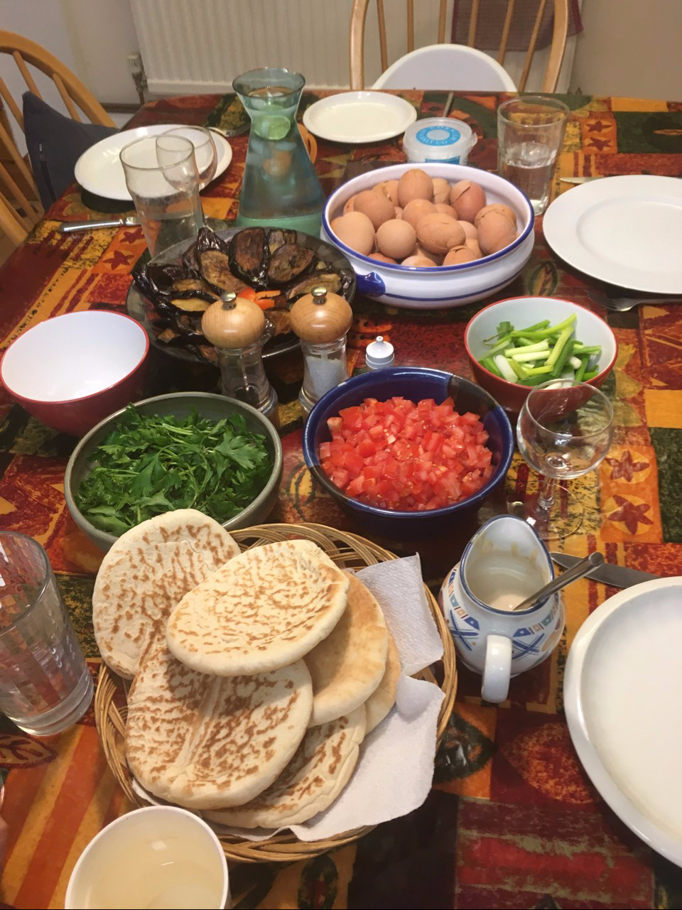A table laid with red eggs, babinjan, chopped tomatoes, parsley, spring onions and pita