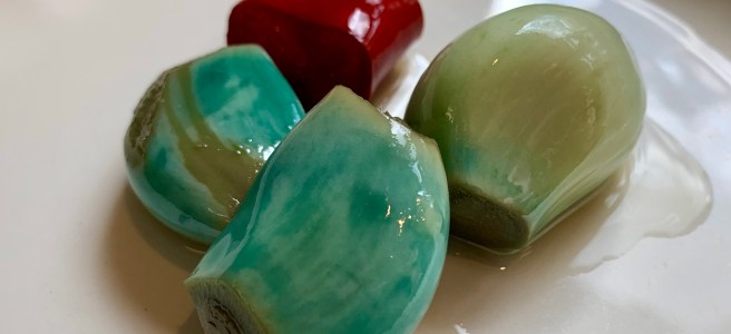 pickled garlic, a green-blue colour, with a slice of red chilli in the background